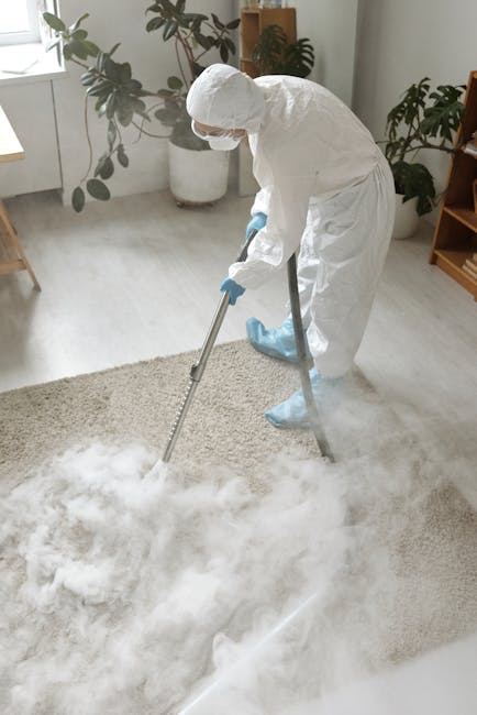 A person is kneeling on a patterned rug in a residential setting, preparing a yellow and black vacuum cleaner for use. The individual, dressed in a beige shirt and blue jeans, is opening the vacuum's